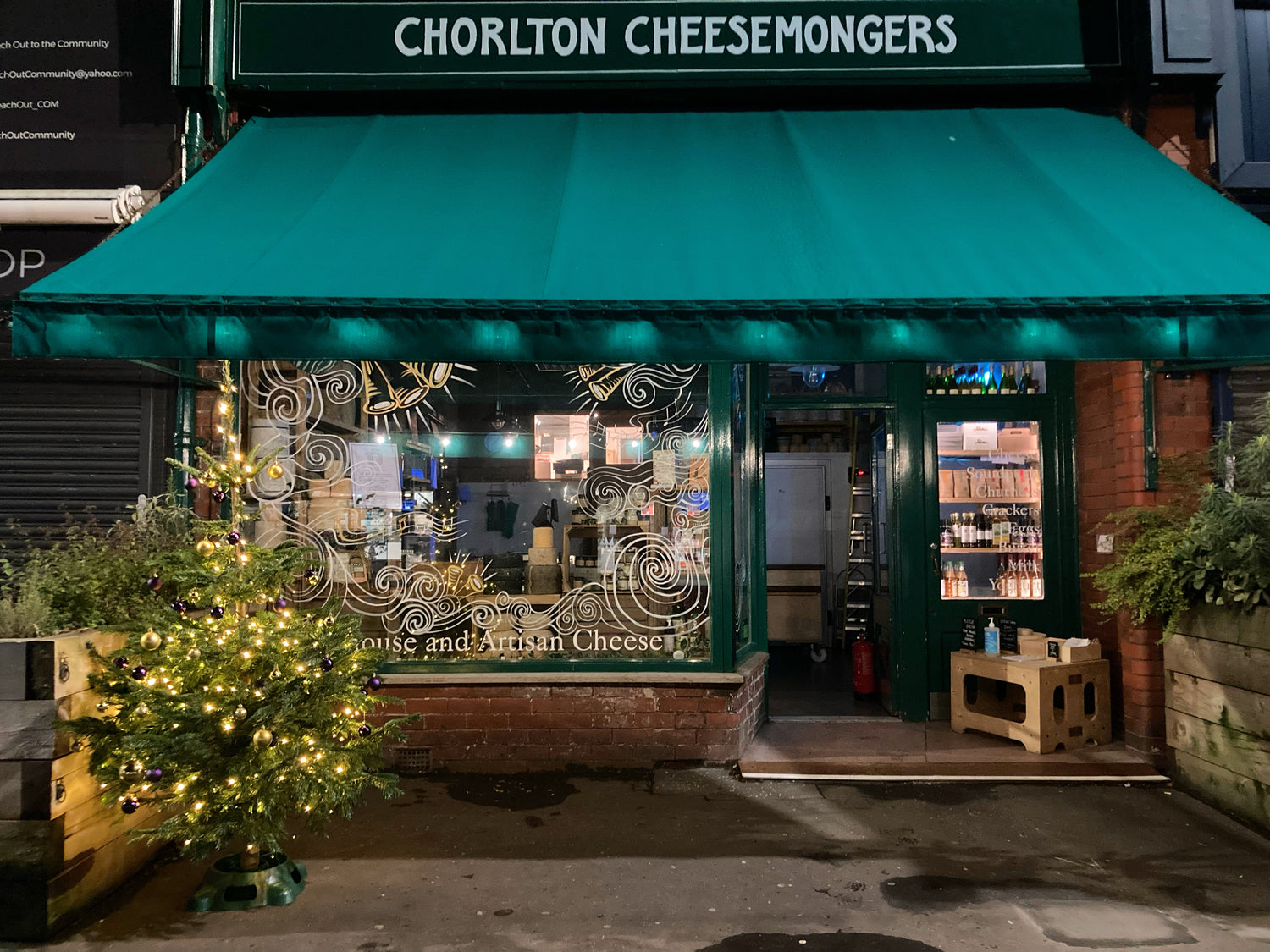 Early morning exterior of the shop, lit for Christmas, with dark green canopy, Christmas tree and lights