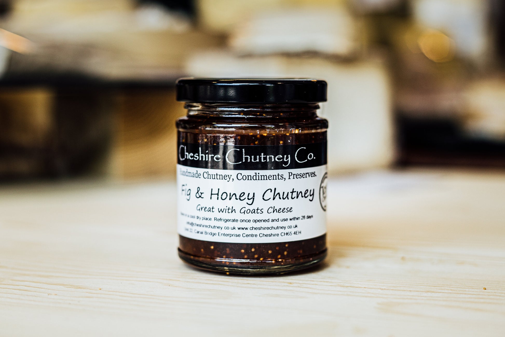 A jar of textured Fig & Honey Chutney in traditional packaging, with the emblem 'great with goats cheese'.