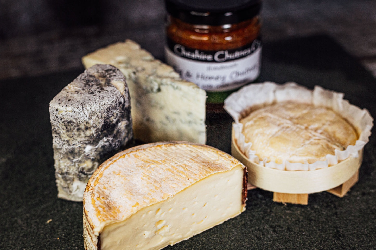 A close up of 4 cheeses - little roll right soft and gooey, charcoal dusted Dorstone, crumbly Brunswick blue, and St just in it's rustic wood basket