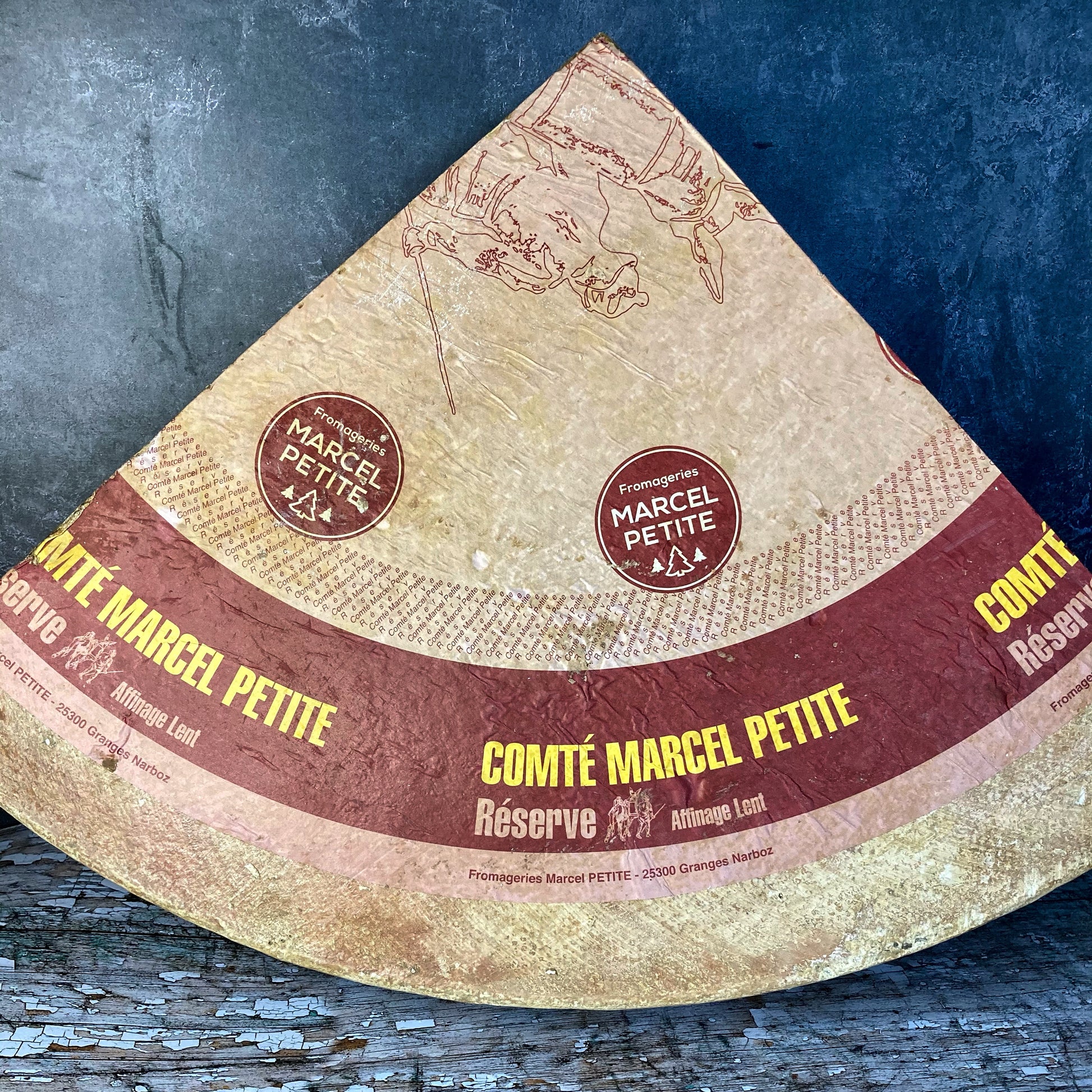 An enormous quarter of Comtè cheese, with it's distinctive red band of Marcel Petite, and the Green bell denoting it as Comtè extra.